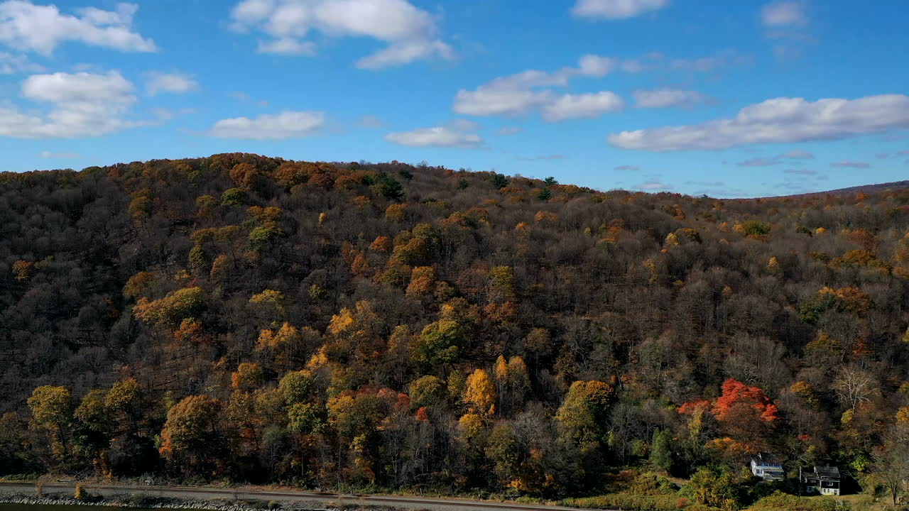 An aerial timelapse of the south side of the Mid-Hudson Bridge as the camera pans right - dolly out, viewing the Highland Landing on the west bank of the Hudson River, cars - trains on a sunny day.