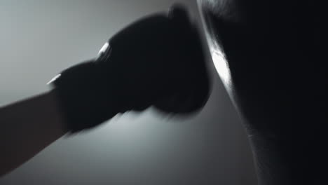 a gloved hand repeatedly punches a boxing bag in a dark setting