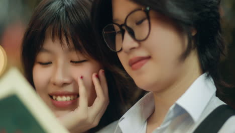 asian girl friends smile and talk as they read book, closeup bokeh background