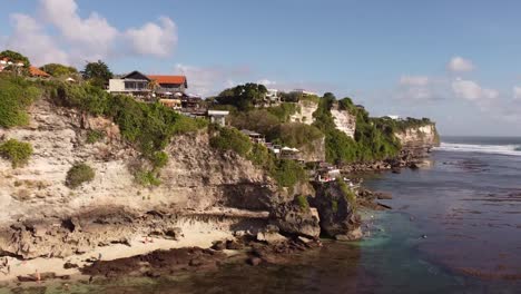 rising drone shot of suluban beach on bali indonesia with visible cliff in afternoon sun in the summer during low tide and big waves