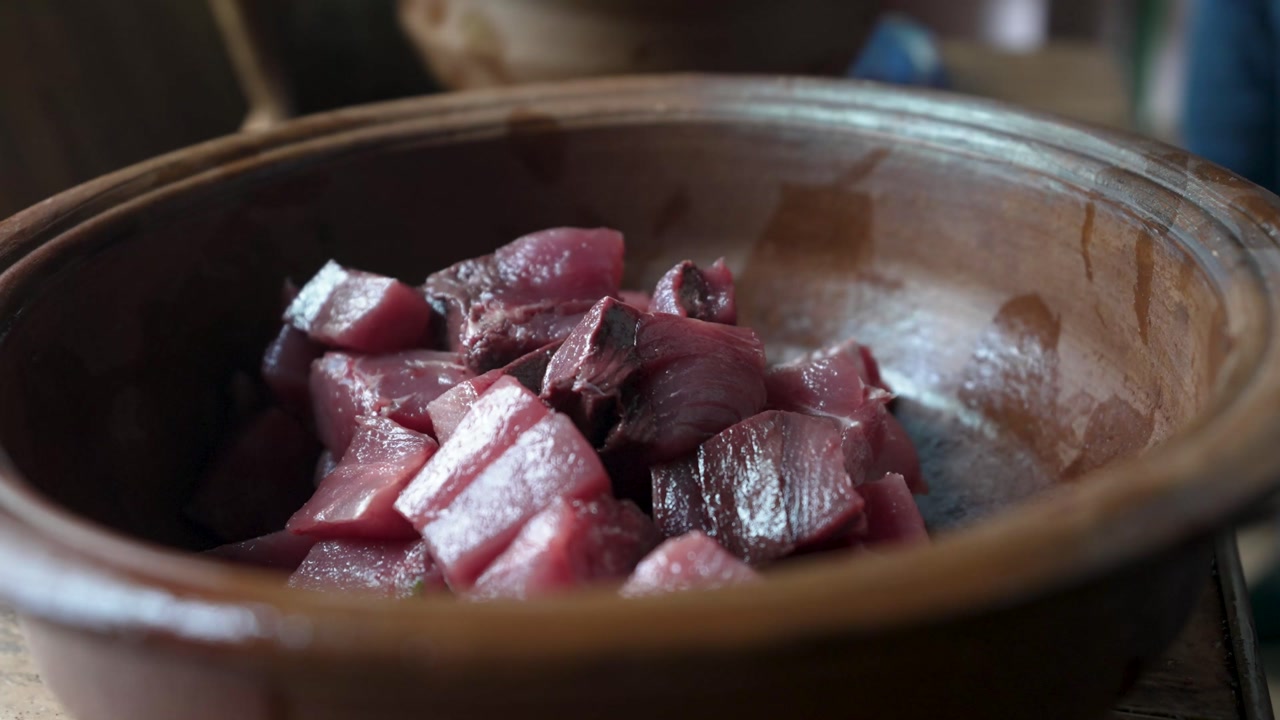 Close-up of fresh tuna cubes falling into a clay pot, capturing the moment of food preparation with a rustic, traditional touch.
