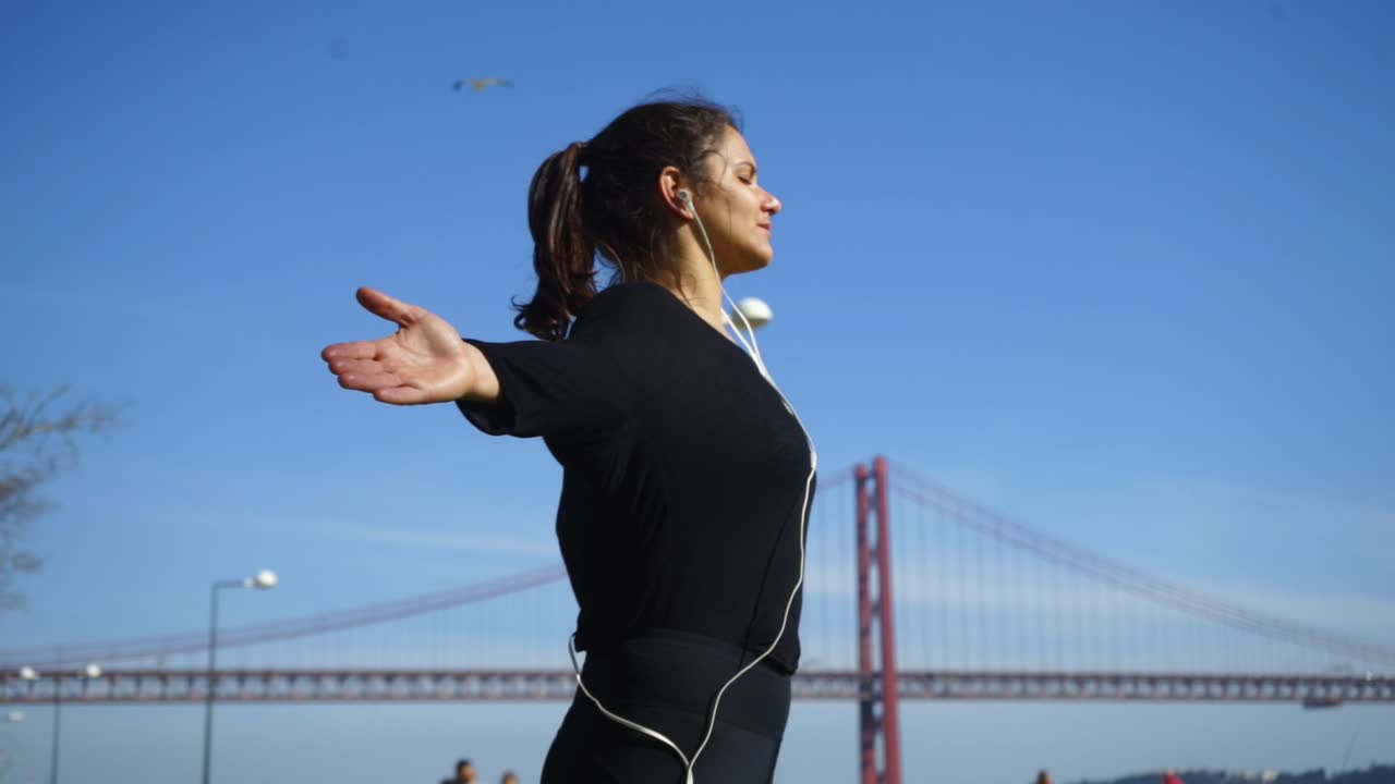mujer joven con los ojos cerrados y los brazos abiertos haciendo ejercicio en el parque