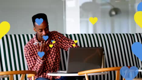 Multiple-yellow-and-blue-heart-icons-floating-against-african-american-man-talking-on-smartphone