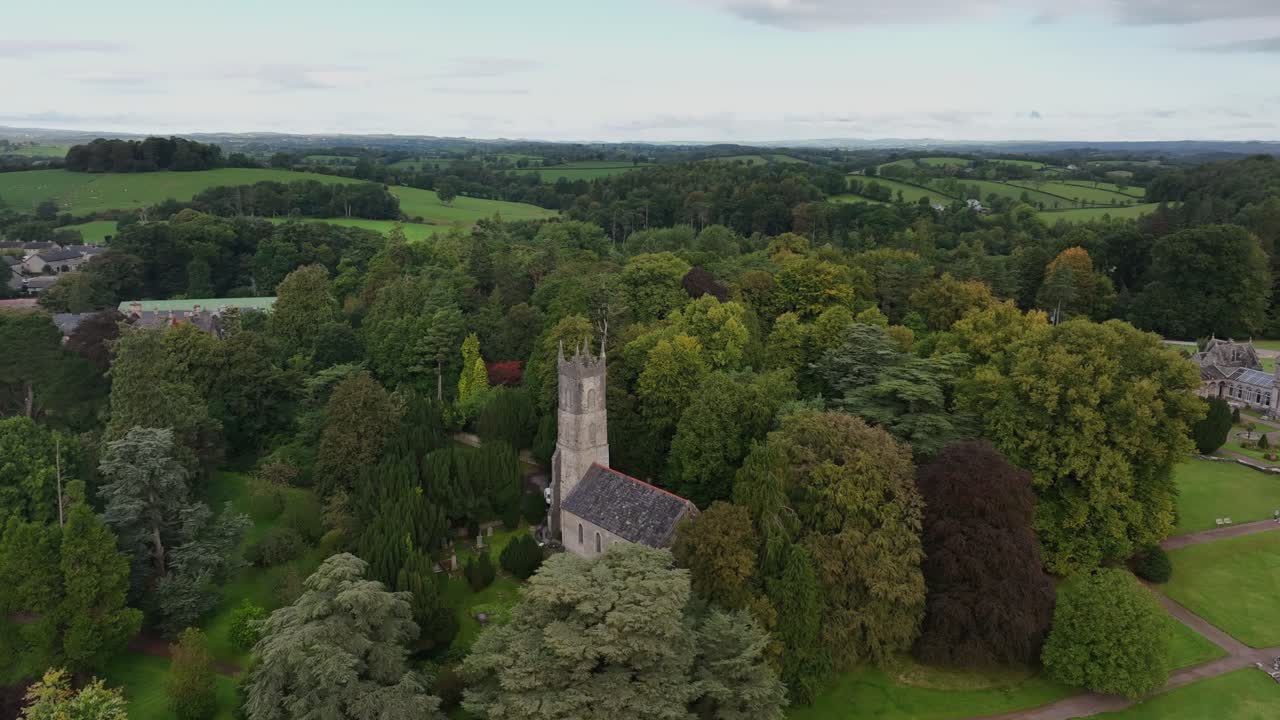 St. Salvator's Church, Glaslough, County Monaghan, Ireland, September 2022. Drone zoom out and orbit clockwise keeping building surrounded by trees framed at center.