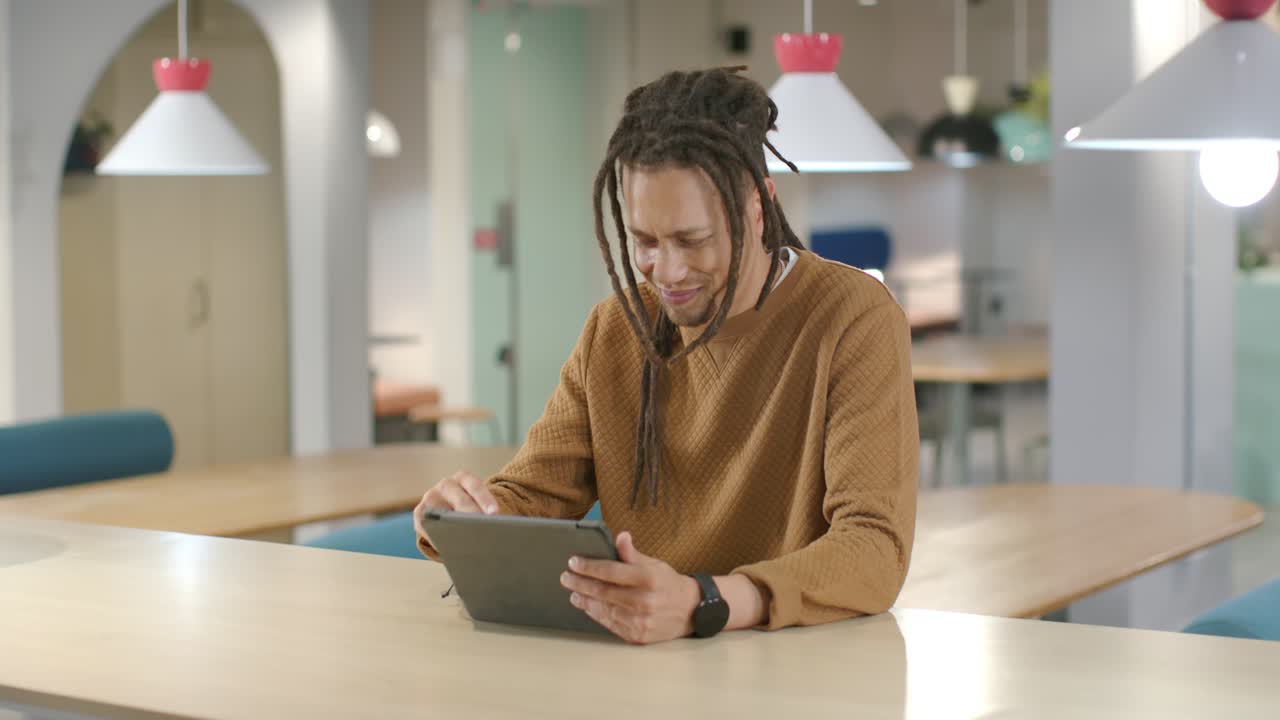 African American man in his 30s scanning tablet, tapping with stylus at communal wooden table