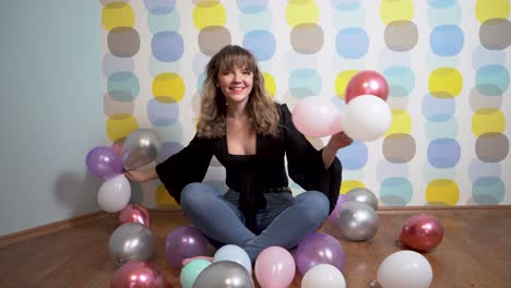 Junge-Frau-Sitzt-Um-Luftballons-Herum-Und-Wirft-Vor-Buntem-Hintergrund-Luftballons-In-Die-Kamera