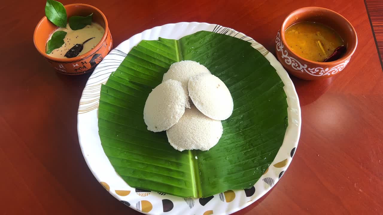 Serving Idly one by one on a banana leaf with chutney and sambar