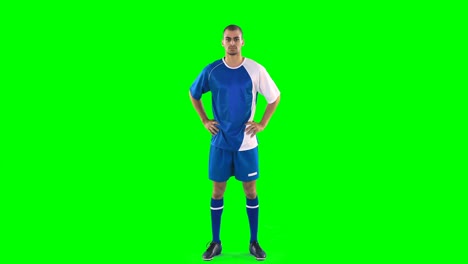 jugador de fútbol seguro de sí mismo de pie contra la pantalla verde