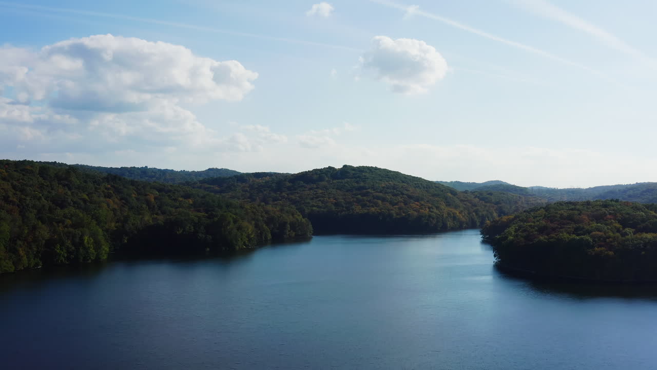 Aerial drone fly-in of the New Croton Reservoir, showcasing its deep blue waters surrounded by lush, colorful forested hills in Westchester County, New York.