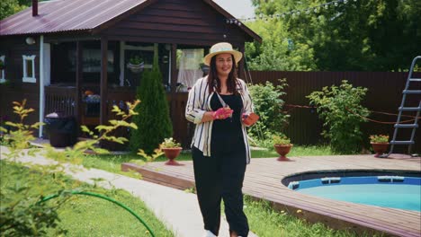 woman in casual attire walking towards a wooden house with a garden and swimming pool in summer