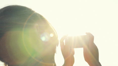 mujer tomando fotografías usando un teléfono móvil al atardecer