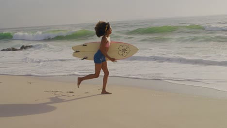 vista lateral de una surfista afroamericana corriendo con una tabla de surf en la playa 4vista lateral de afric