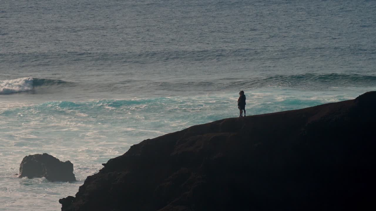 A young couple walks hand in hand along a rugged volcanic cliff overlooking the Atlantic Ocean in Lanzarote, Canary Islands, Spain.