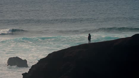 a young couple walks hand in hand along a rugged volcanic cliff overlooking the atlantic ocean in lanzarote, canary islands, spain.
