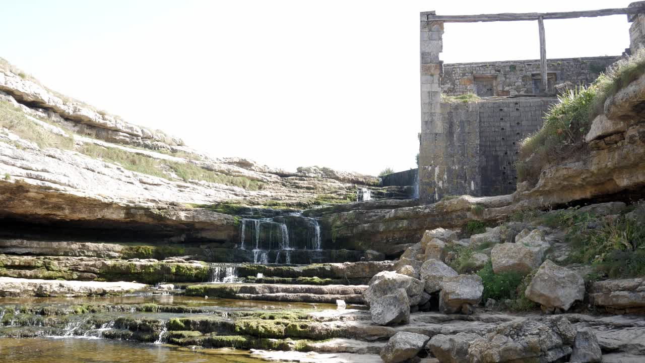 Ruins of Bolao Windmill near waterfalls, located in Cantabria, Spain, under sunlight