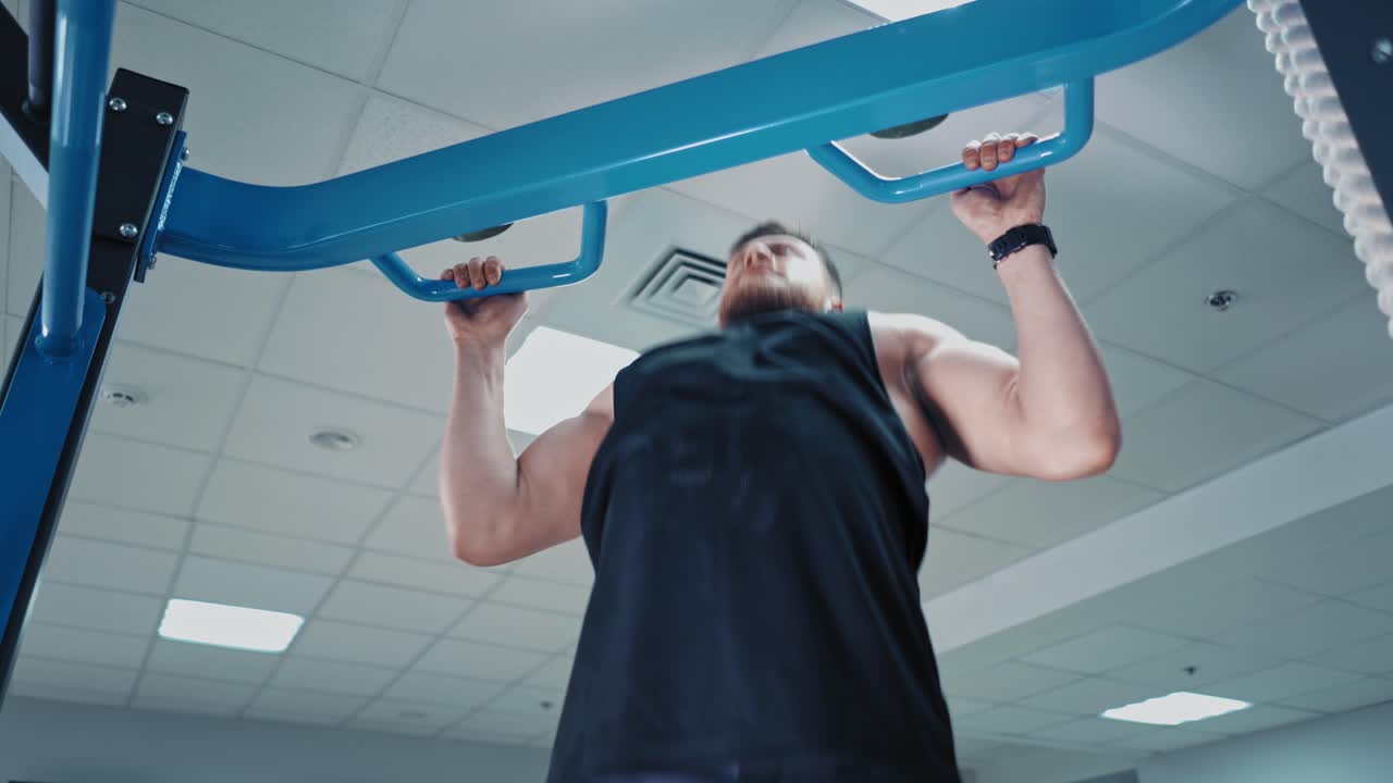 Close-up of concentrated young athlete tightening his body. Strong muscular man exercising fitness training to his arms during workout in the gym.