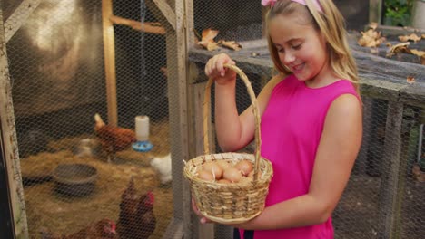 happy caucasian girl holding basket of eggs standing by hen house in garden