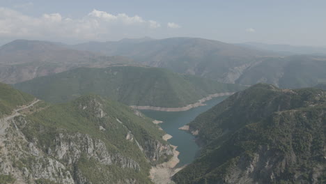 drone shot flying over the mountains near the koman lake in albania on a sunny day with clouds with blue water and a green valley log