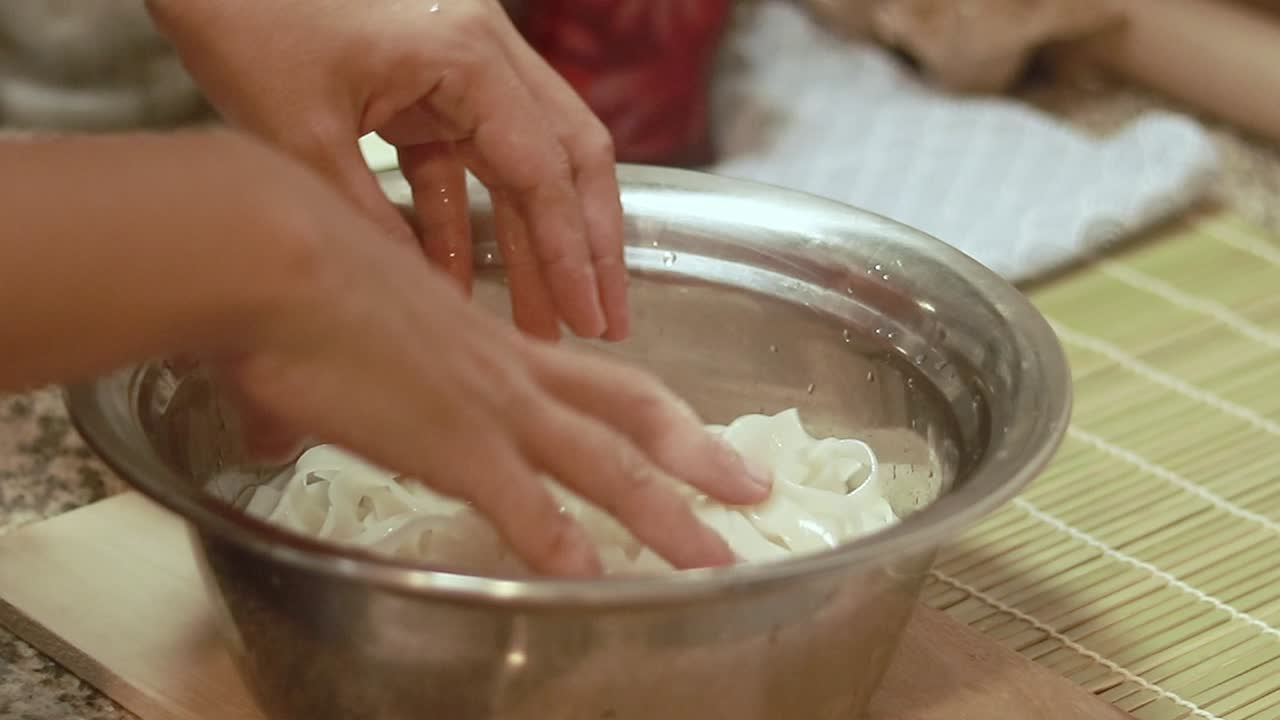 Soaking and rinsing flat rice noodles in a bowl of water in a kitchen counter, preparing it for cooking