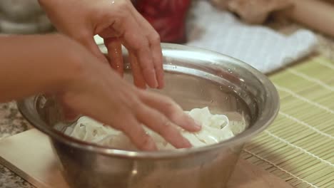 soaking and rinsing flat rice noodles in a bowl of water in a kitchen counter, preparing it for cooking