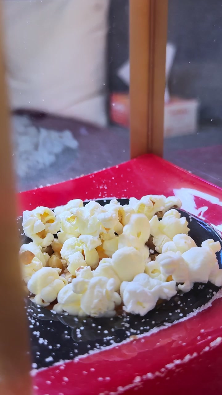 Du popcorn fraîchement éclaté dans un bol noir à l'intérieur d'une machine à popcorn rouge. Ces images très détaillées capturent la texture de cette collation dans un cadre de cinéma.