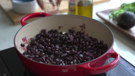 verter agua en una olla de frijoles negros cocidos antes de agregar condimentos dos latas de frijolas arroz plátano aguacate cebolla roja y cilantro