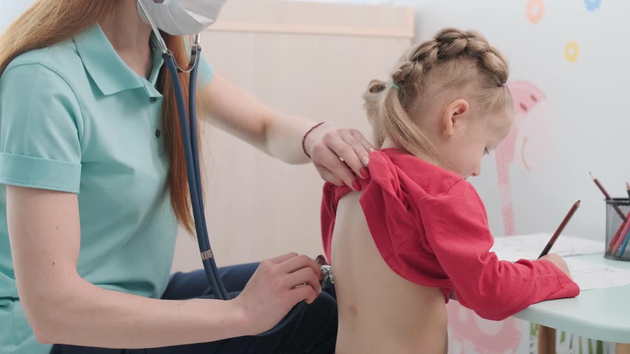 Ein Kinderarzt in einem Krankenhaus untersucht und hört ein kleines Mädchen mit einem Stethoskop ab.