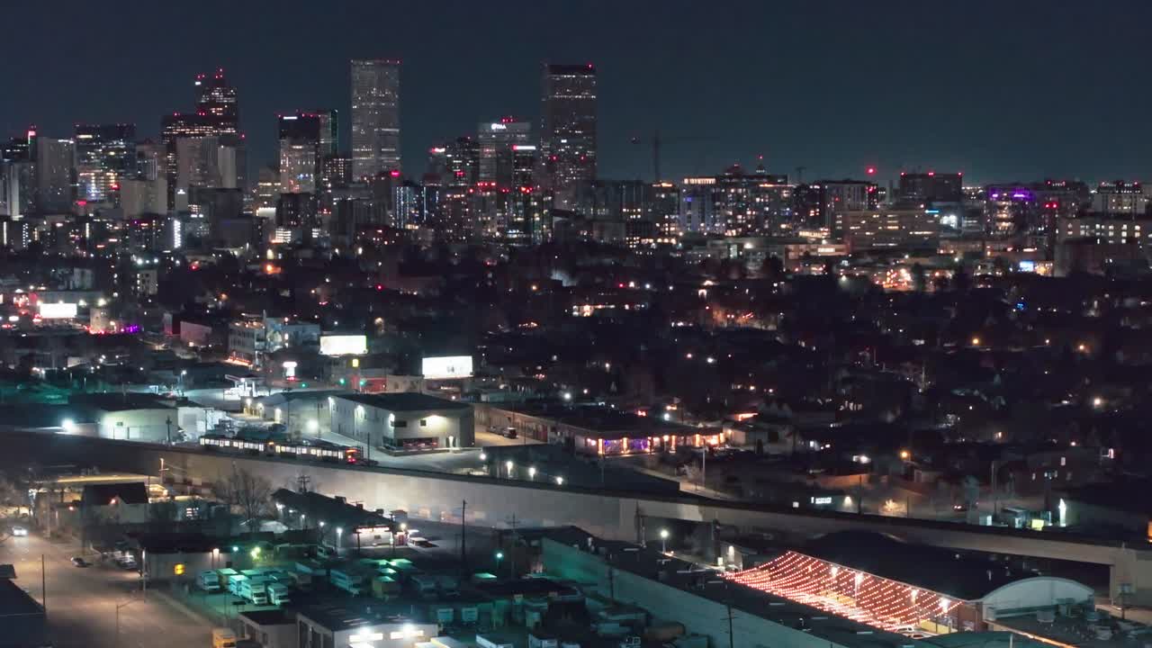 Drone pullsback as commuter tram rail train drives in front of dense urban industrial zone at night