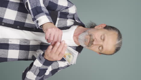 Vertical-video-of-Old-man-counting-money-looking-at-camera.