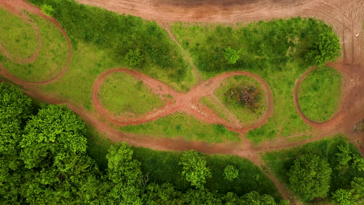 toma aérea del signo infinito moto pista de tierra con césped y árboles alrededor