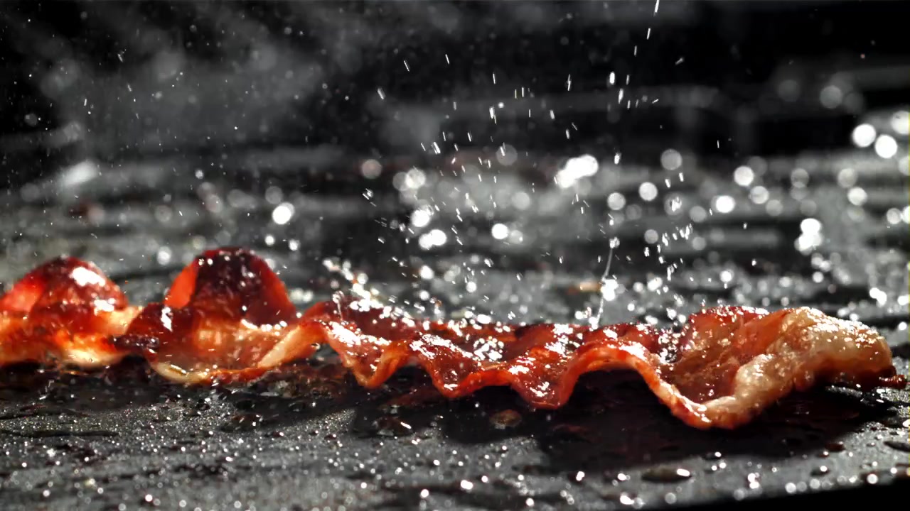 Baconstrimmel falder og syder på varm stegeplade i slowmotion