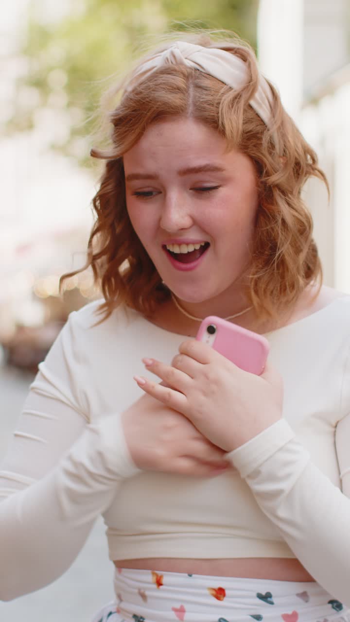 Ung kvinde bruger mobil smartphone til at fejre sejr, god besked, nyheder udendørs i byens gade