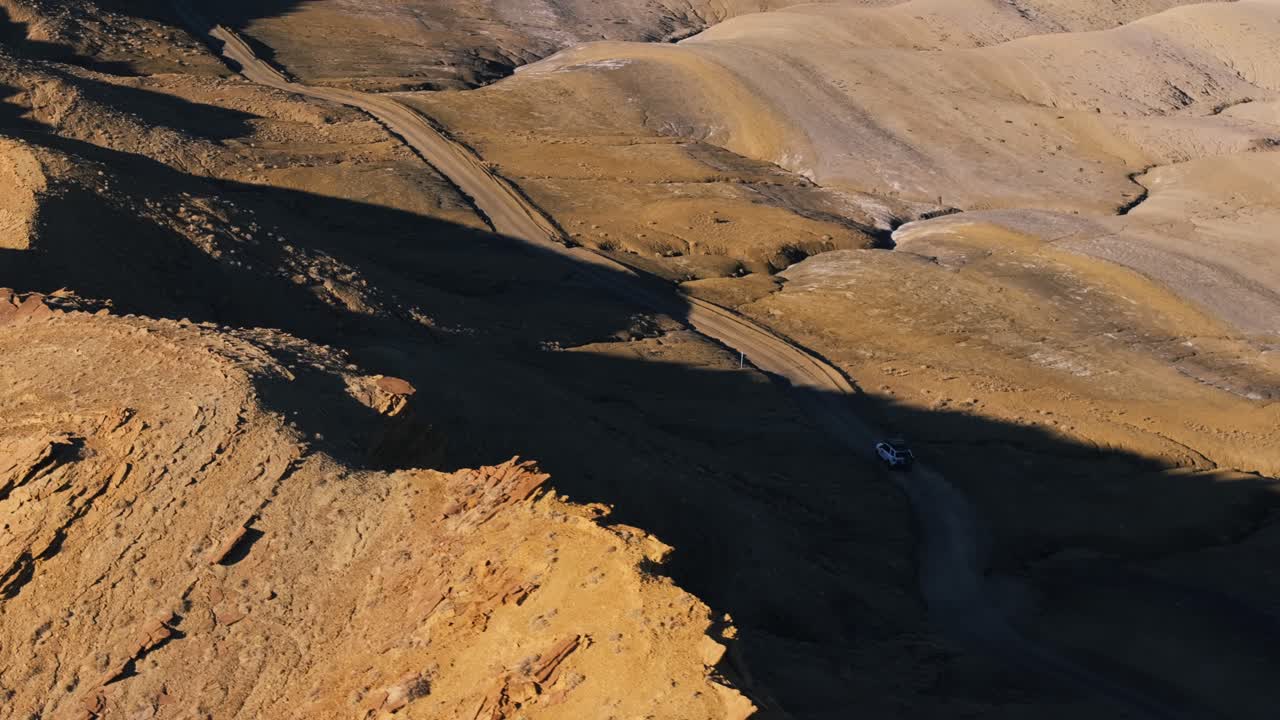 미국 유타주 공장 버트 문스케이프 (factory butte moonscape) 를 가로질러 멀리 떨어진 야생 도로를 따라 운전하는 고립된 차량