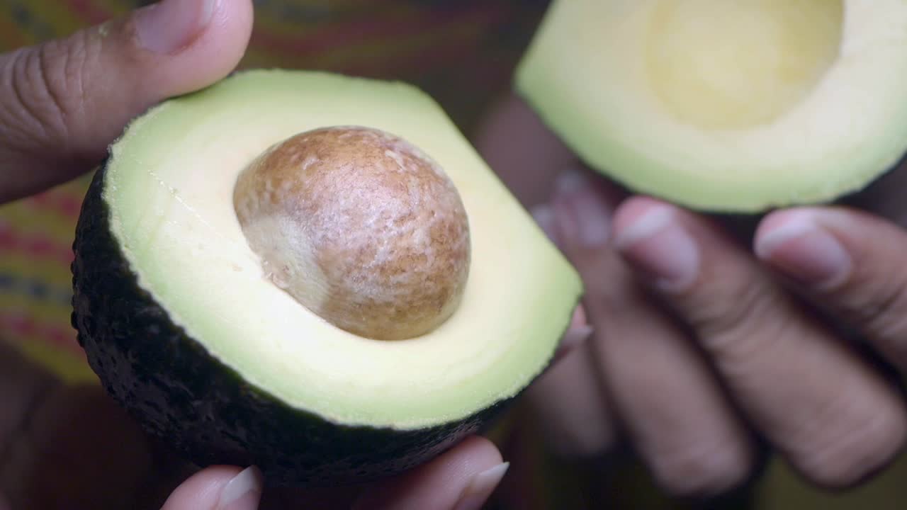 Close-up de Mãos Segurando um Abacate Fresco Cortado ao Meio com Caroço