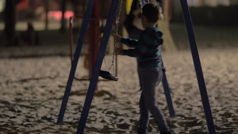 niño divirtiéndose con columpios vacíos en el patio de recreo por la noche
