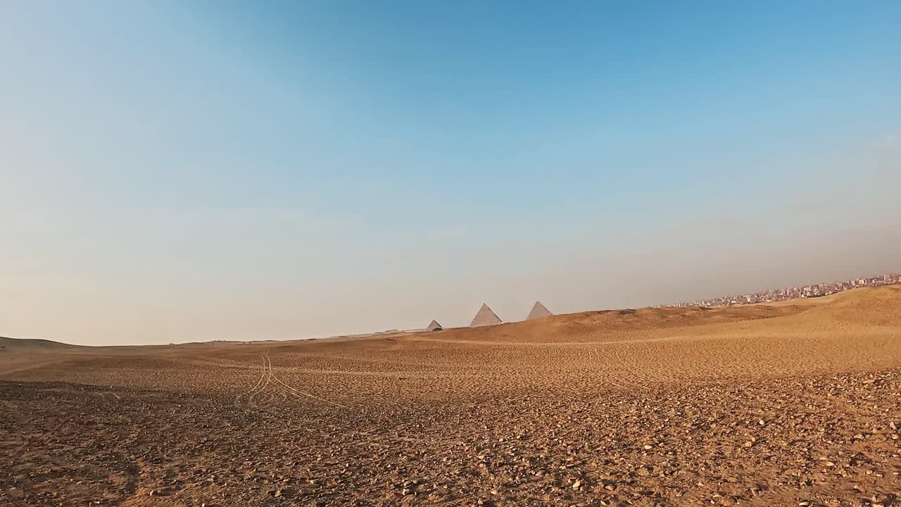 Muž jedoucí na čtyřkolce pouštní krajinou směrem k pyramidám