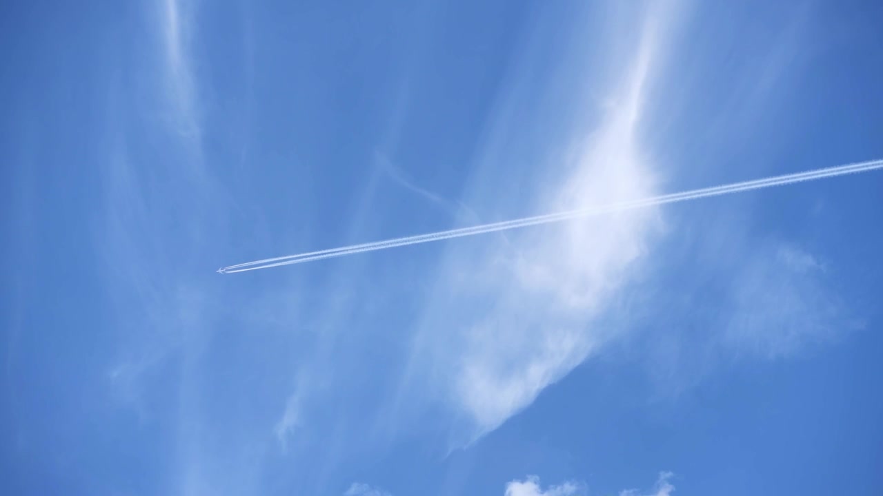 薄い雲が浮かぶ明るい青空を背景にジェット機が飛行機雲を作る。旅行や航空をテーマにしたプロジェクトに最適。
