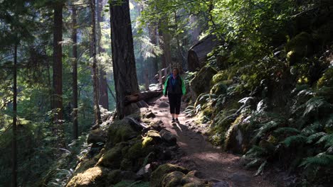 senior woman walks down a forest path with light beams shining through the canopy
