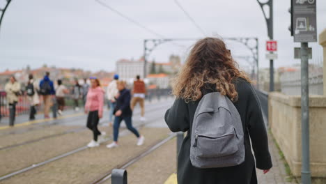 woman with backpack walking on a city bridge