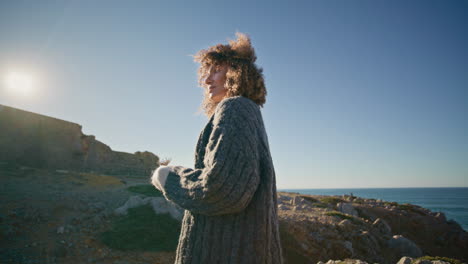 autumn lady standing ocean cliff at sunshine back view. model holding dry flower