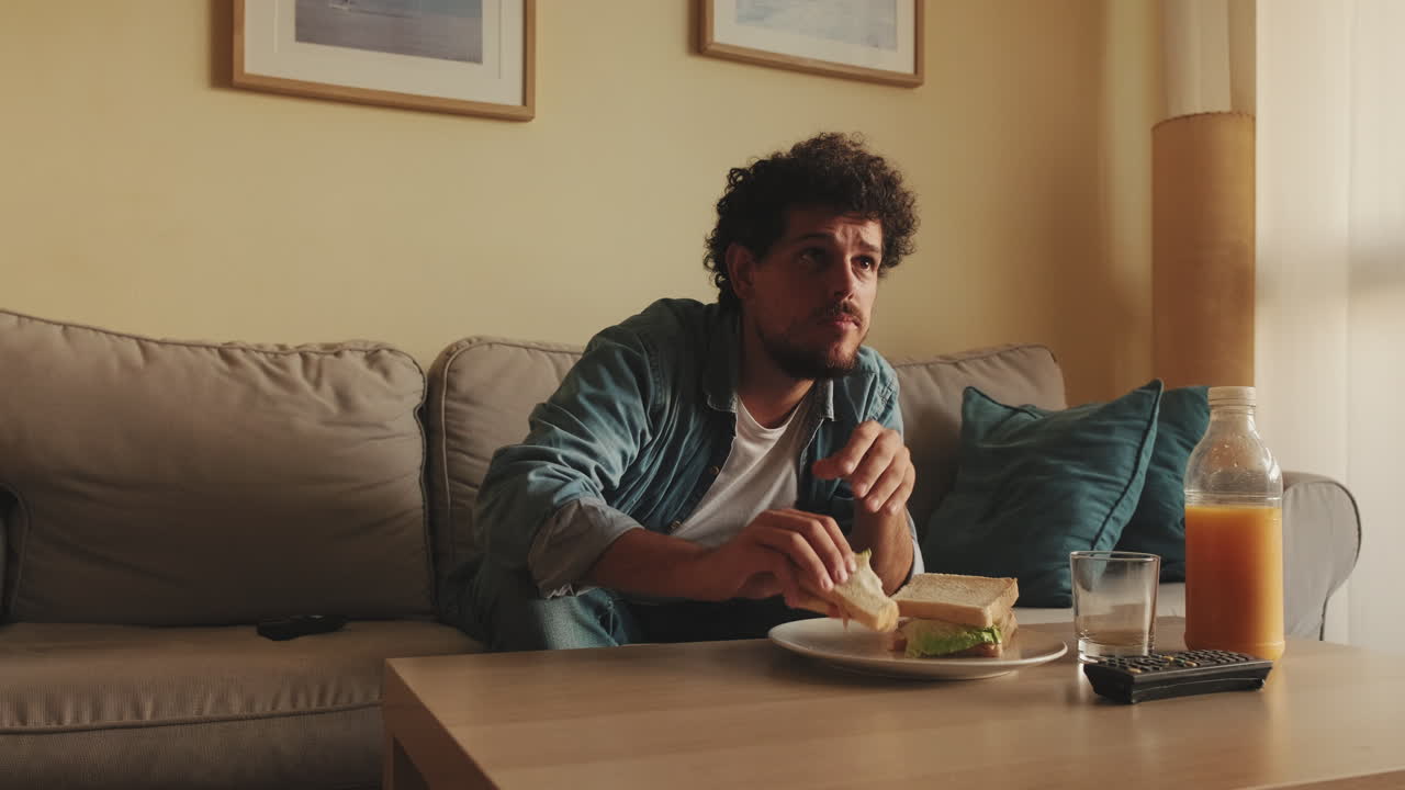 Man eating a sandwich while watching TV