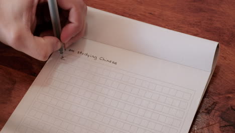 man hands writing i’m studying chinese in mandarin chinese characters in a notebook over a wooden table