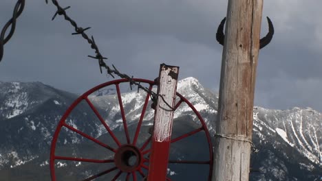 Mittlere-Aufnahme-Von-Western-Mountains,-Rotem-Wagenrad,-Stacheldraht-Und-Rinderhörnern,-Die-An-Eine-Stange-Geheftet-Sind