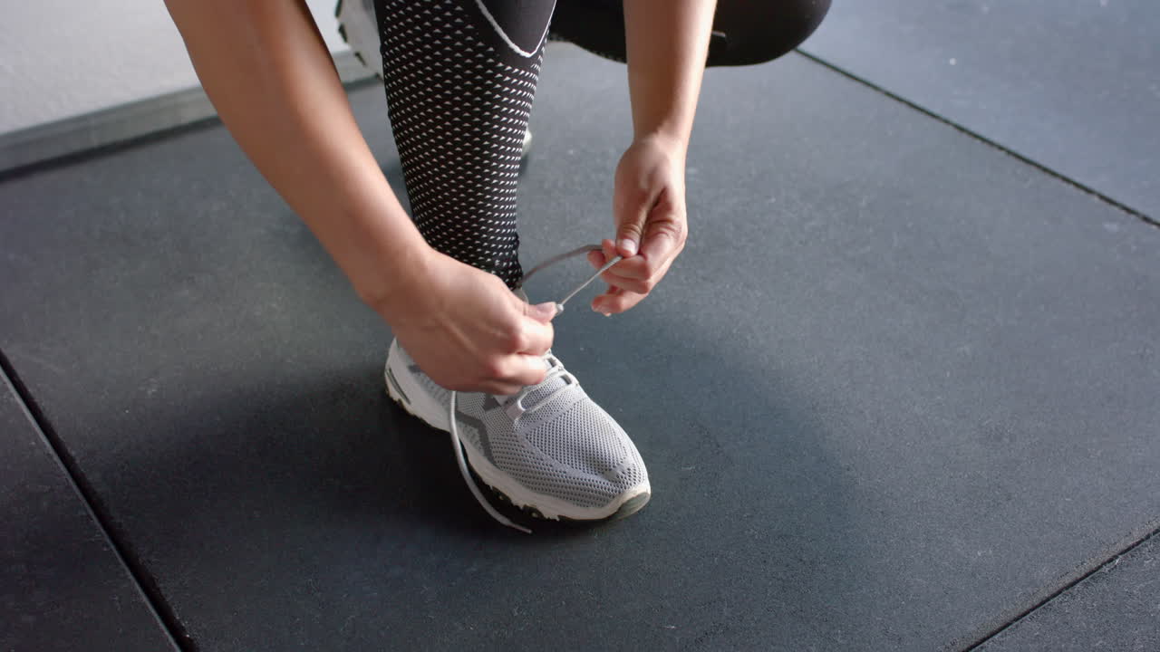 Donna che si allaccia le scarpe, preparandosi per l'allenamento in palestra, indossa scarpe sportive.