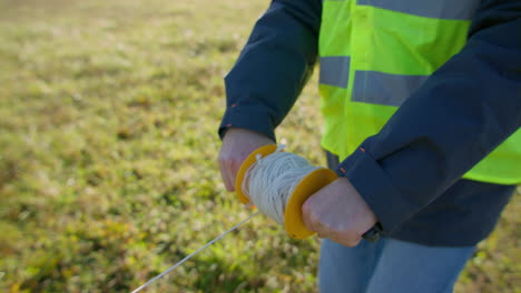 male engineer deploying a wire across the grassy field from handheld spool of cable on a rod, handheld closeup