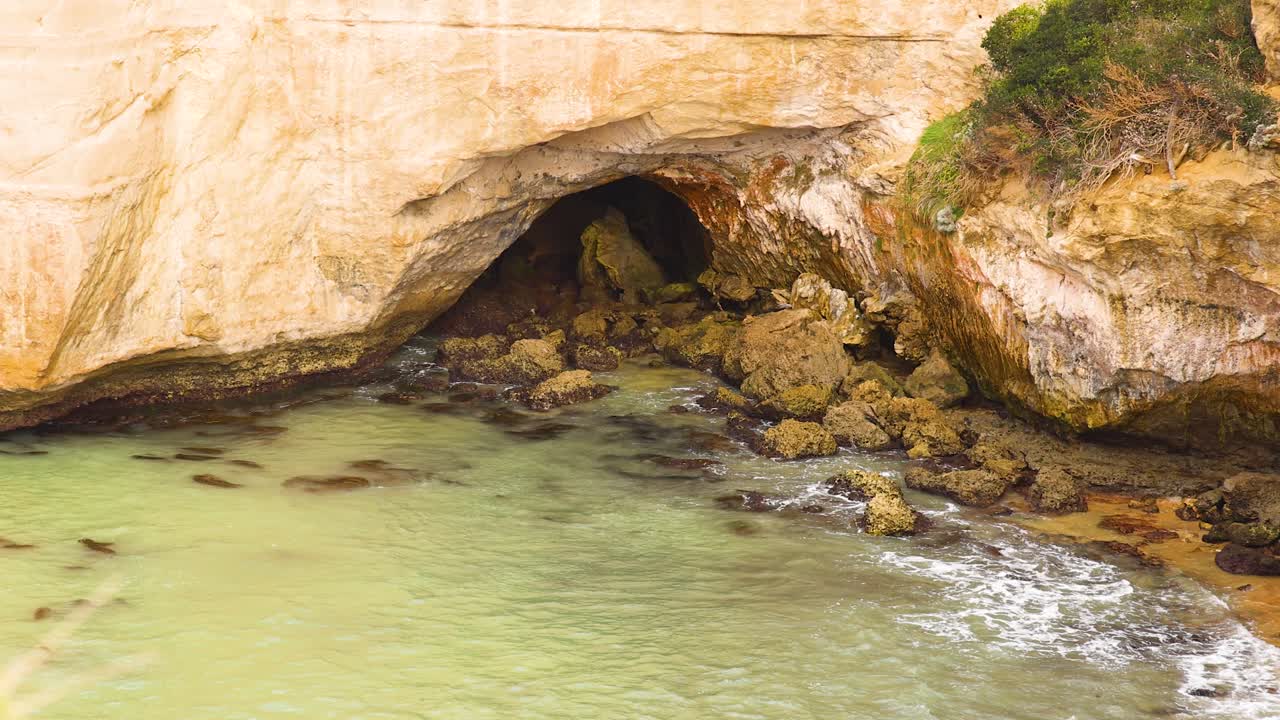 Waves gently lap against rocky cliffs at Loch Ard Gorge, Port Campbell. Soft lighting enhances the natural beauty of the coastal landscape