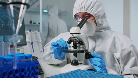 científico con traje de ppe mirando muestras bajo el microscopio