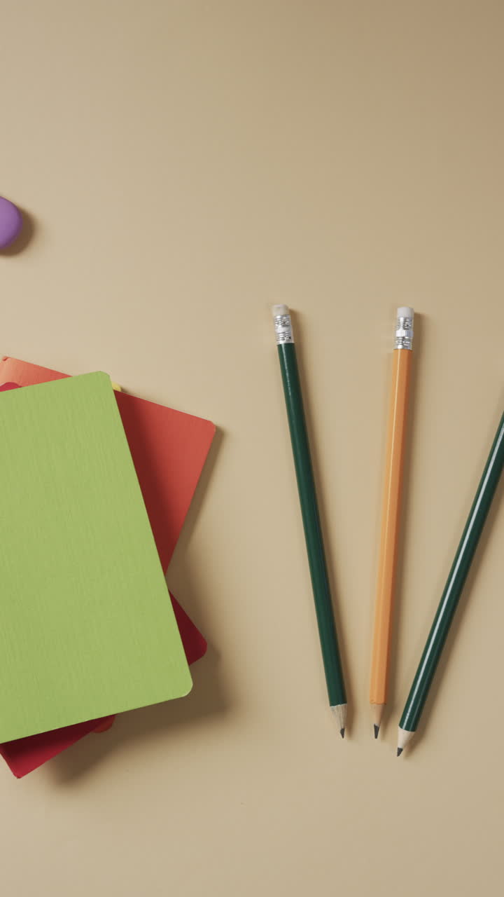 Vertical video of overhead view of school stationery on beige background, in slow motion