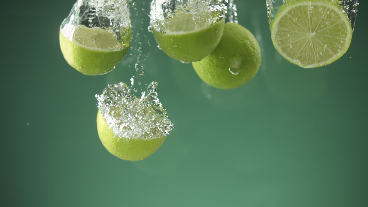 cámara lenta de limas frescas en rodajas cayendo al agua sobre fondo verde