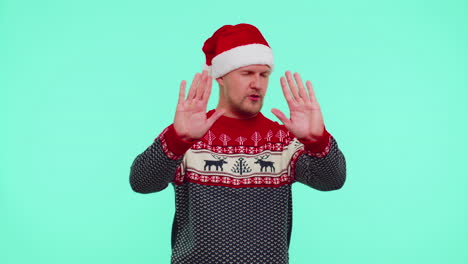 man in christmas sweater covering ears and gesturing no, avoiding advice ignoring unpleasant noise